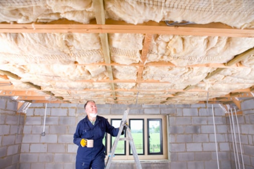 Man in coveralls drinking coffee on ladder and looking up at ceiling insulation