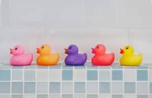 Canards en plastique jouets de salle de bain colorés posés sur un rebord en mosaïque bleue