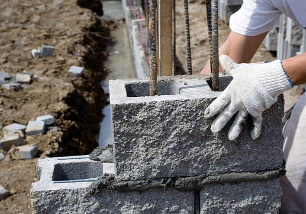 Artisan qui manipule un bloc de béton perforé avec joints verticaux