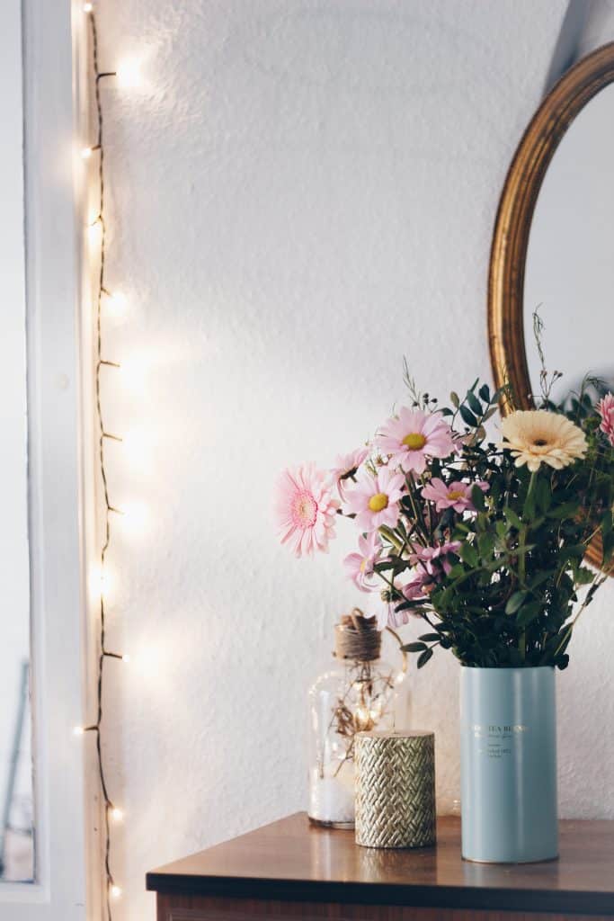 Guirlande lumineuse placée sur le chambranle d'une porte, à côté d'une table sur laquelle est posé un bouquet de fleurs